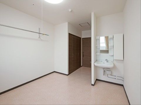 白を基調とした個室タイプの居室である。上部にハンガーポールが設置されており、床はフローリングとなっている。