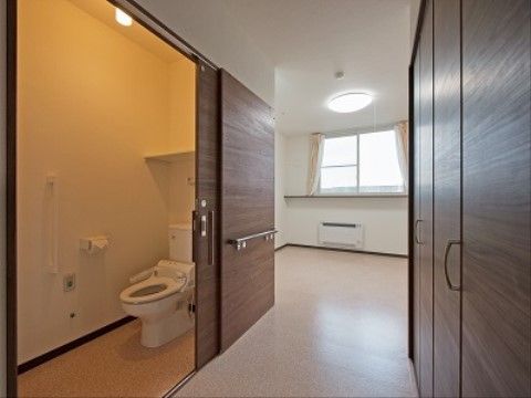 居室に温水洗浄機能付きの洋式トイレが設置されている。壁には、手すりやナースコールが取り付けられている。