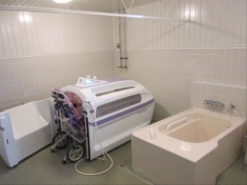 介護浴槽とシンプルな浴槽が並んで設置された浴室である。床と壁は白を基調としたタイル張りとなっている。