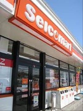 オレンジ色の看板が特徴的なコンビニエンスストアである。ガラス張りの入口横に、ごみ箱が複数置かれている。