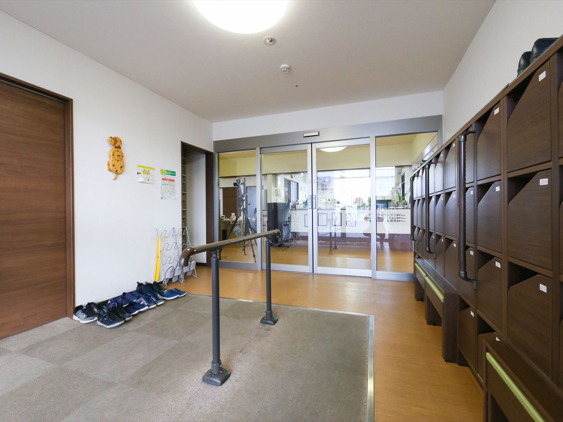 玄関には入居者様おひとりずつの靴箱が設置されている。靴箱の近くの土間部分の中央には、茶色の手すりがある。