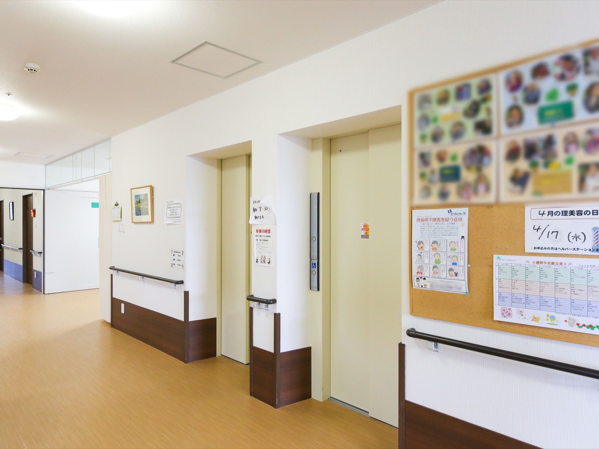 エレベーターが２基設置されている。乗降口の横には、その週の献立や理美容の予定、入居者様の写真が貼られている。