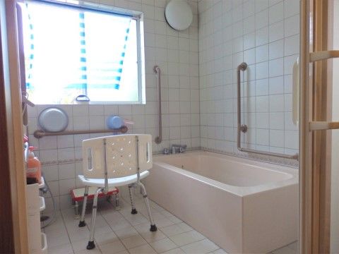 白を基調としており、窓からの陽射しが明るい浴室である。浴槽の周囲には、立ち座りに安全な手すりが設置されている。