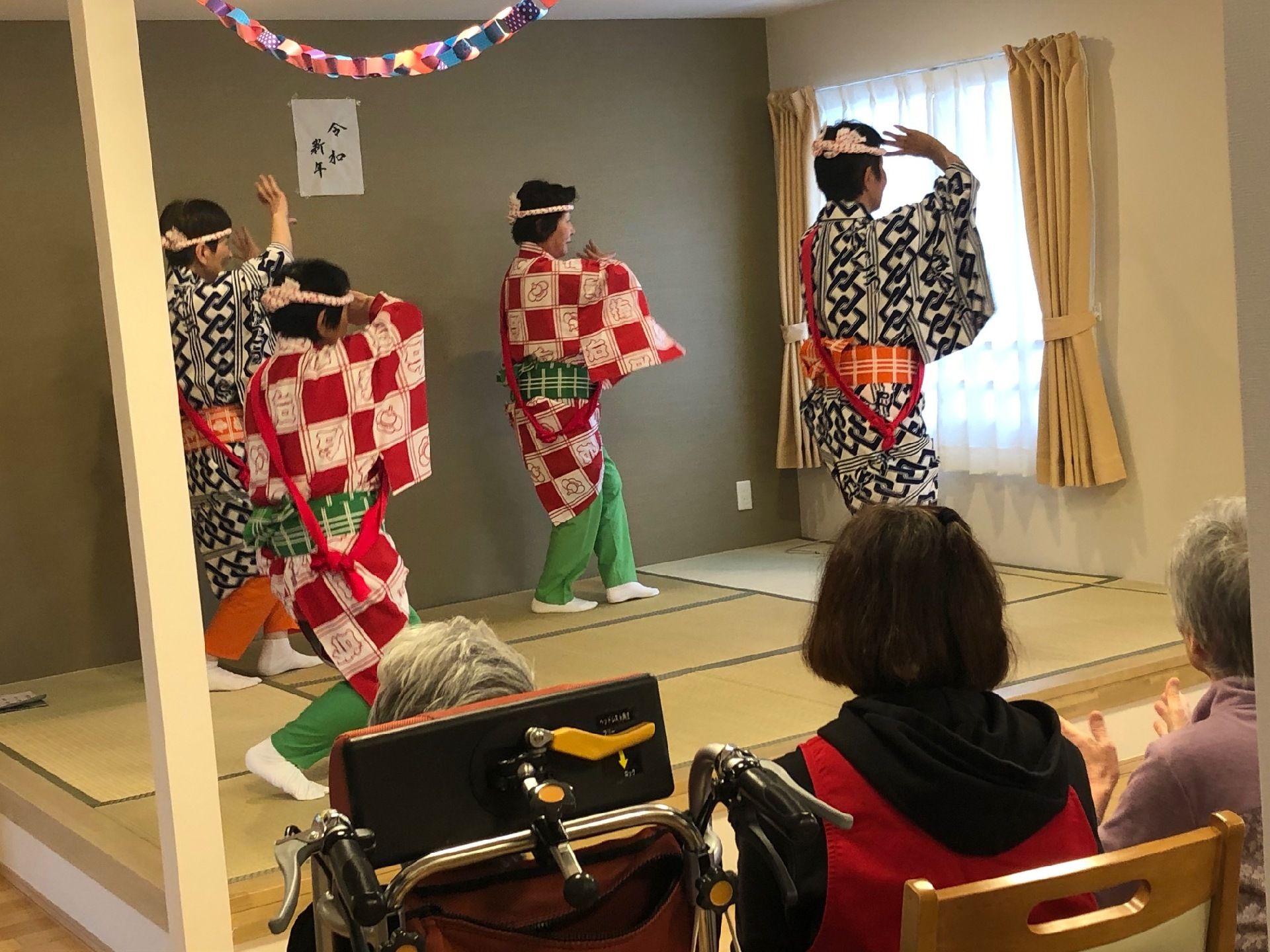 衣装を来て伝統舞踊を披露する演者と、手拍子を取りながら鑑賞する入居者様