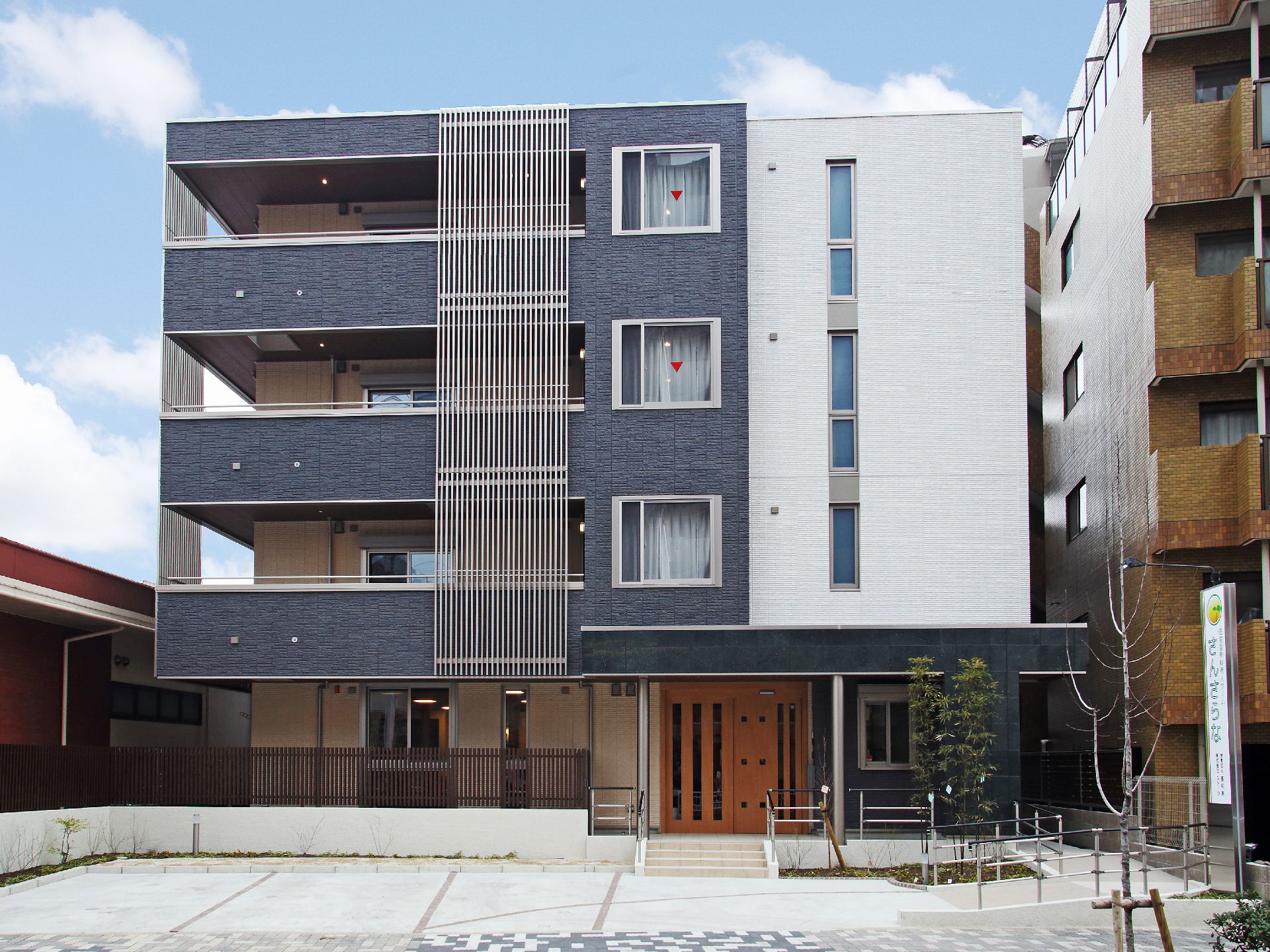 黒とグレーを基調とした外観。4階建ての施設の前面に駐車場が完備。駐車場から玄関まではスロープで移動可能。