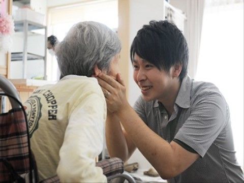入居者と楽しそうな表情で向き合い、様子を見る男性の施設職員