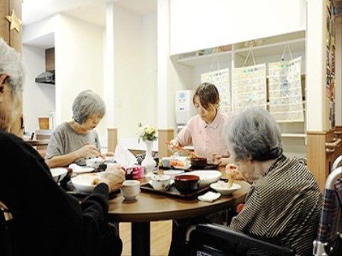 4人の男女が各々、一つの食卓を囲んで、食事をしている。奥には、給水機があり、入居者様にも簡単に使用することができるような工夫を行っている。