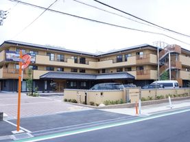 施設は3階建てになっている。車の駐車スペースもあり、その場所は外壁で囲まれている。車も数台が停車している。