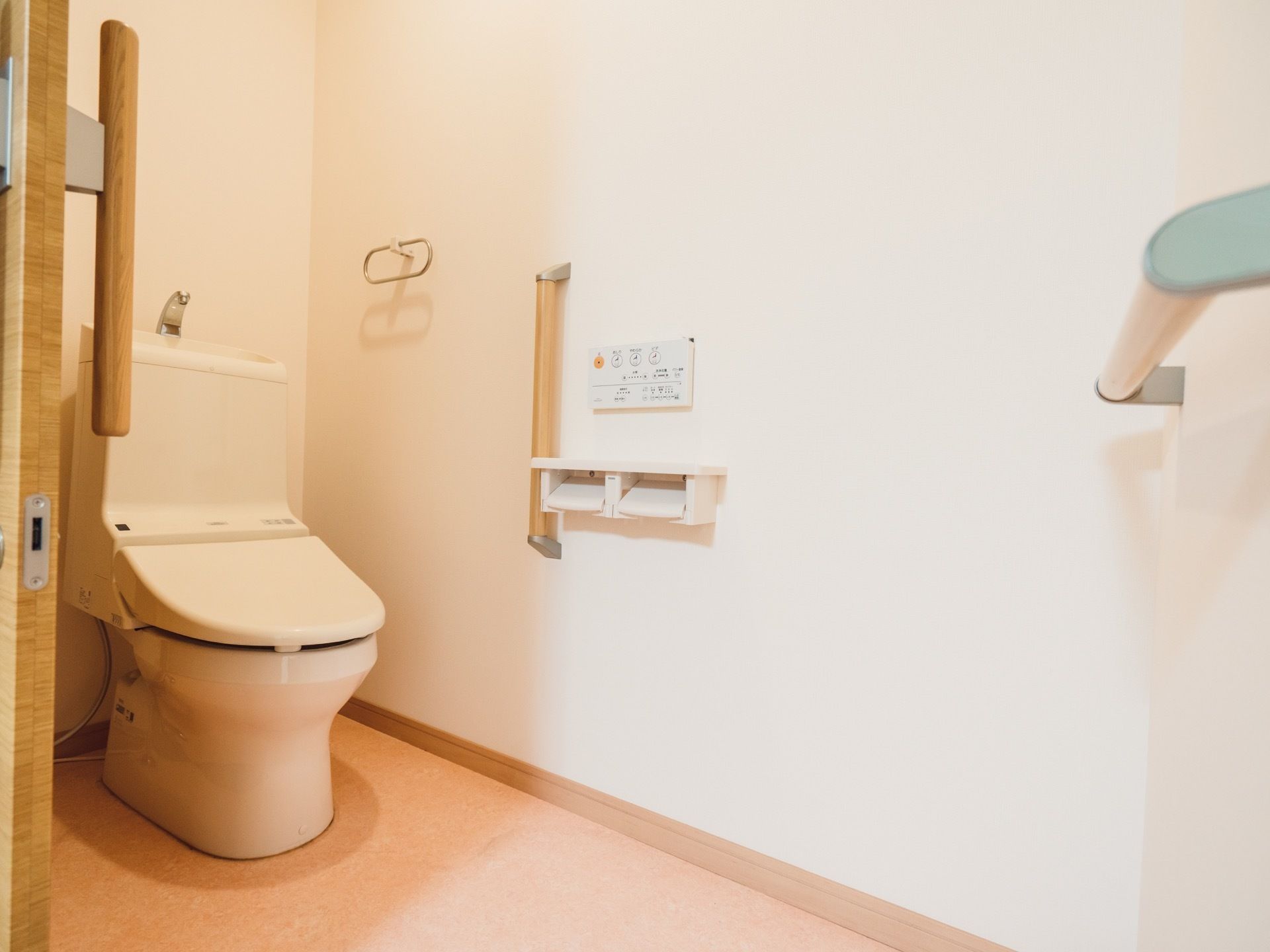 広々とした清潔感のあるトイレである。温水洗浄便座や手すり、タオルハンガーを完備している。ドアは間口の広い引き戸である。