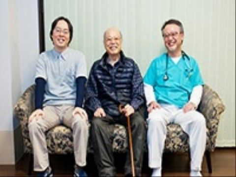 施設スタッフと並んで座り、笑顔でポーズを取る入居者様の写真