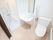 真っ白に掃除された洗面台の奥にシャワールームがある。手前にはトイレがあり、壁に折り畳み式の手すりがある。