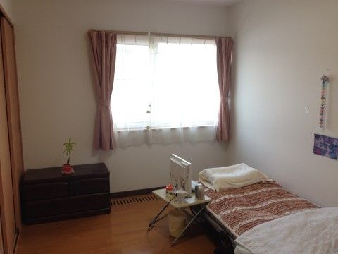 壁は白く、床は茶色のフローリングの部屋だ。ベッドは低めのもので、枕が置かれている。そばには小さなテレビやゴミ箱が設置されている。