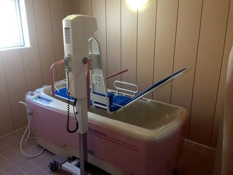 タイル貼りで窓がある浴室に、介助浴槽がある。その脇には横になったまま浴槽に入れる電動式リフトが置かれている。