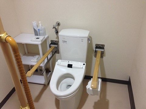 温水洗浄便座があり、左右には上に跳ね上がるひじ置きが付いている。部屋の隅には棚があり、上に消毒液がのっている。