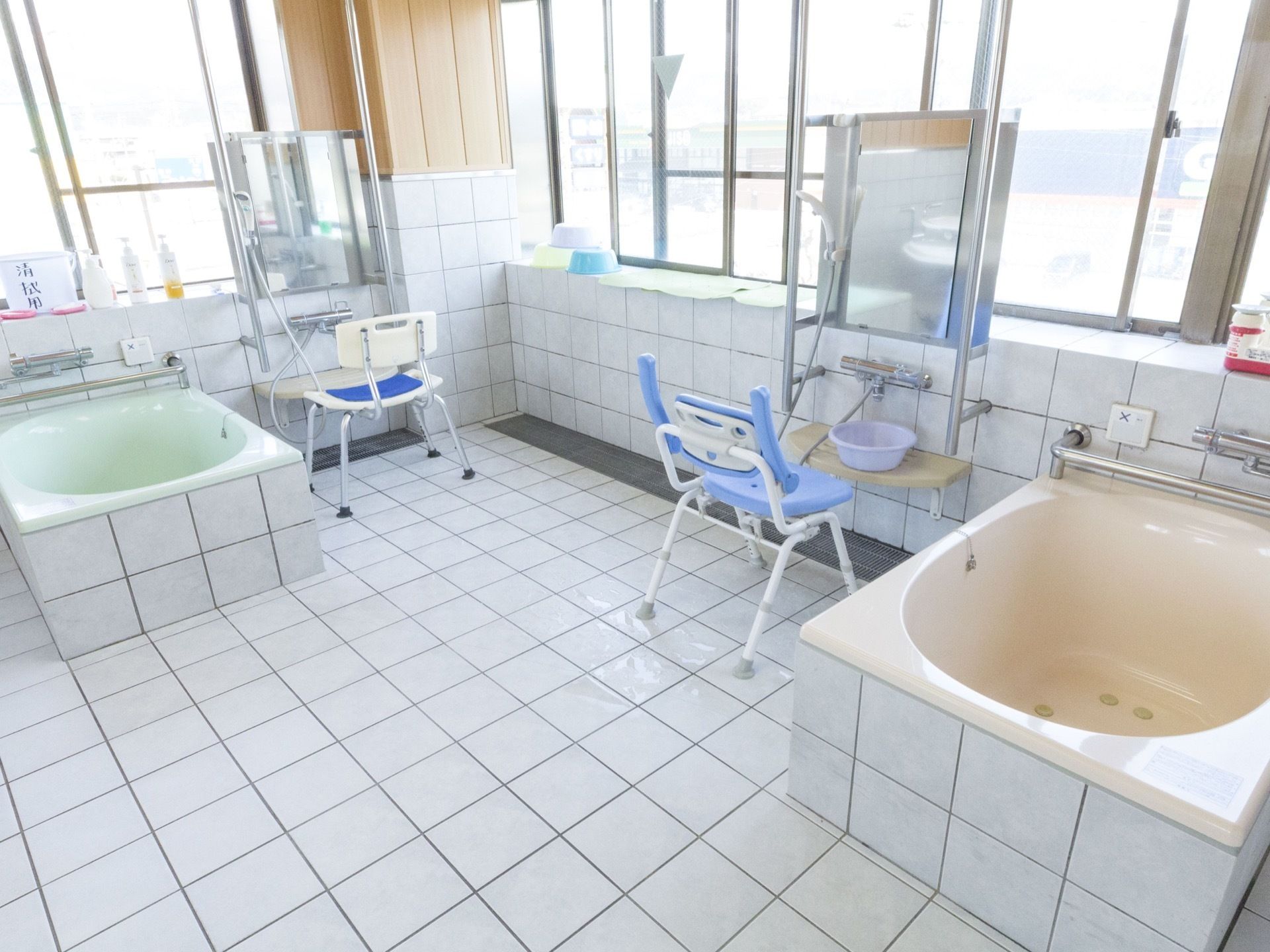 浴室壁には腰高窓が連なっている。壁と床は大きめの白色のタイル貼りである。浴槽はピンクとグリーンの2つある。