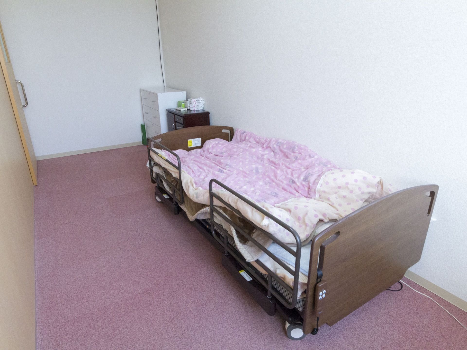 ドア側の壁はドアと同色のうすい茶色である。その他の壁は白色である。居室に入ってすぐ前にチェストが置かれている。