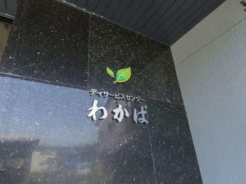 切り出された施設のロゴと文字が貼られた石造りの玄関横の壁