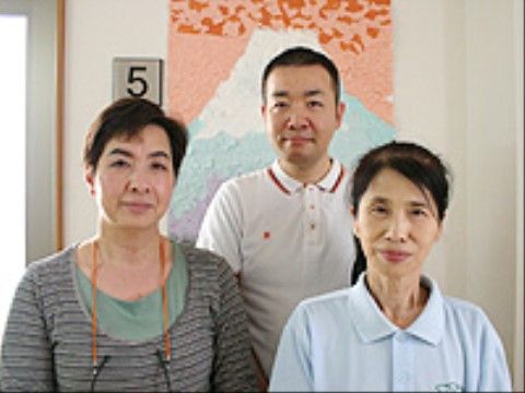 貼り絵作品の前で並んで写真に納まる3人の施設のスタッフ