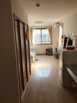 廊下と居住スペースがあり、廊下の側面に冷蔵庫や洗面台などがまとめて設置されている。居住空間には窓があり、ベッドや家具などが置かれている。