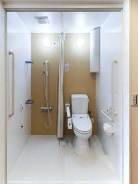 温水洗浄便座の近くには手すりと緊急呼出ボタンが設置されている。カーテンで区切られたスペースにはシャワー設備が設置されている。