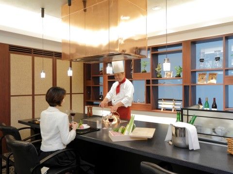 ラウンジではカウンターの中で、白い帽子をかぶったシェフが料理を作っている。背後には棚があり、天井から照明が吊り下げられている。