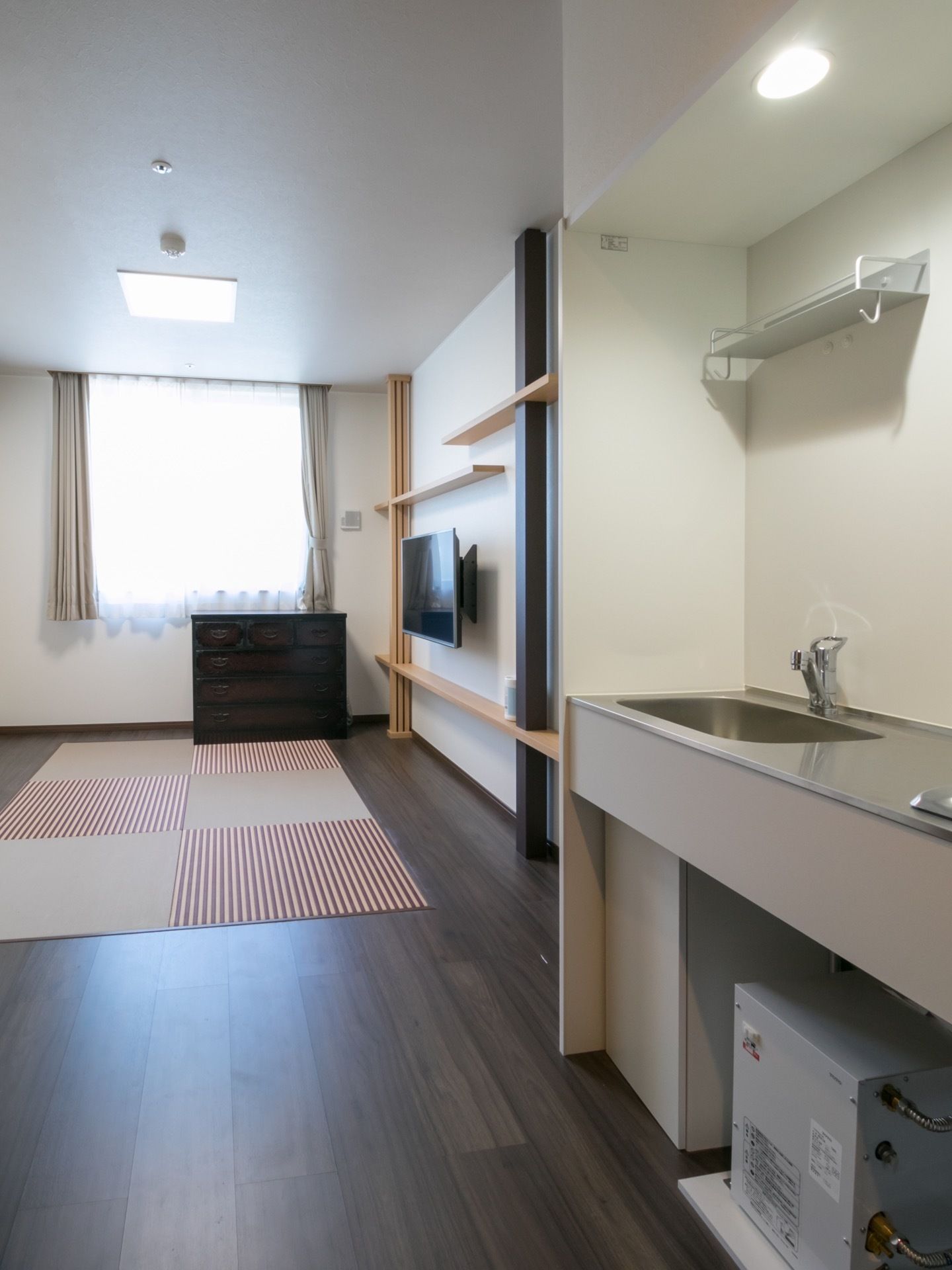 窓があり、外の光が差し込む明るい居室になっている。ミニキッチンがあり、料理を楽しむことができる。白い壁で清潔感のあるスペースである。