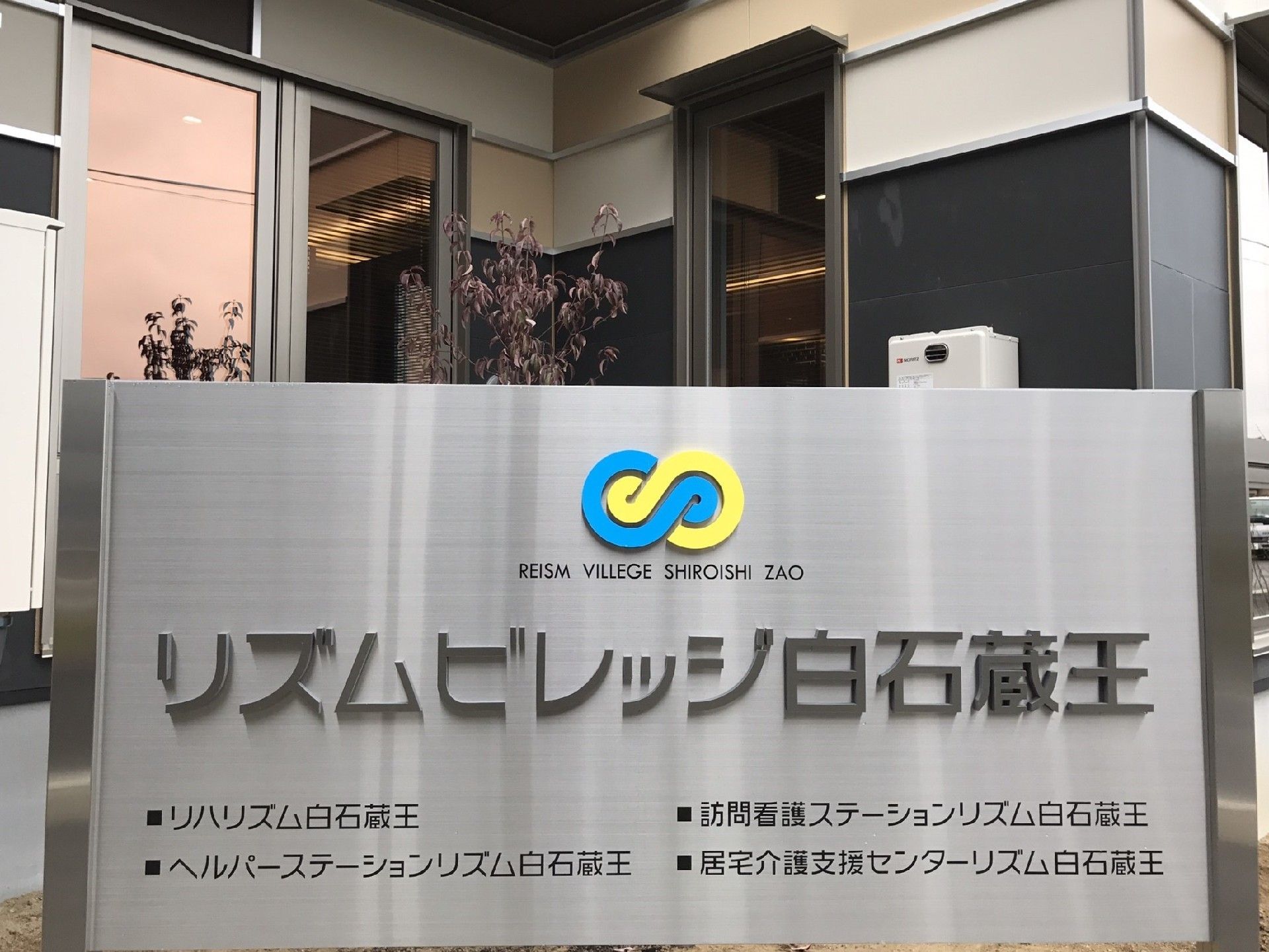 会社のロゴと総合施設名、4つのグループ施設名の書かれたメタル調の看板