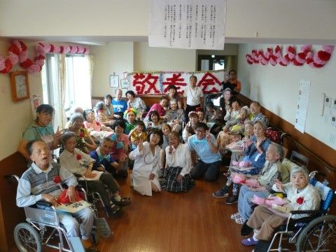 手作りの敬老会の飾りの前に集まり、ポーズを取る大勢の入居者と施設職員