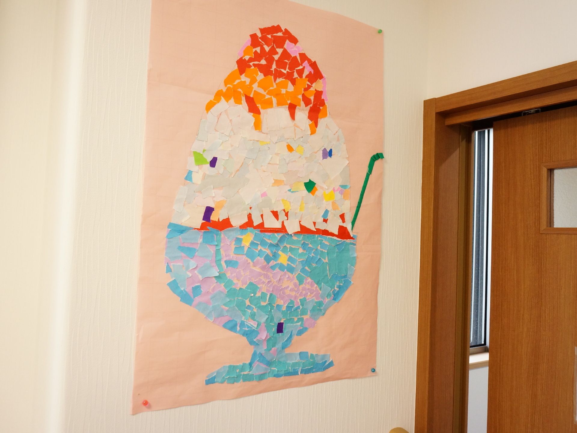 リビングの白い壁にはちぎり絵の作品がカラーピンで貼られている。ベージュ色の紙をベースに様々な色でかき氷が描かれている。