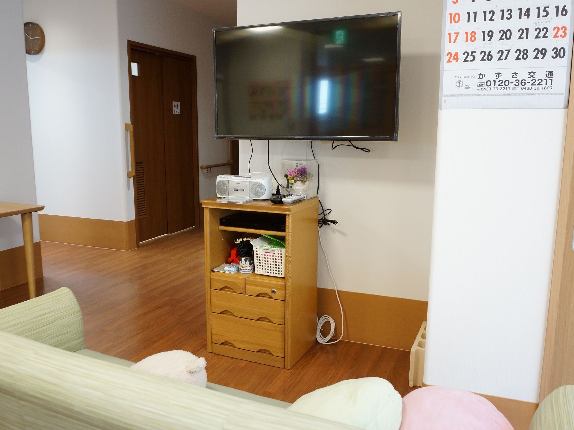 リビングの一角には淡いグリーンのソファーが置かれている。正面の壁にはテレビが設置され、下には木製の収納棚がある。
