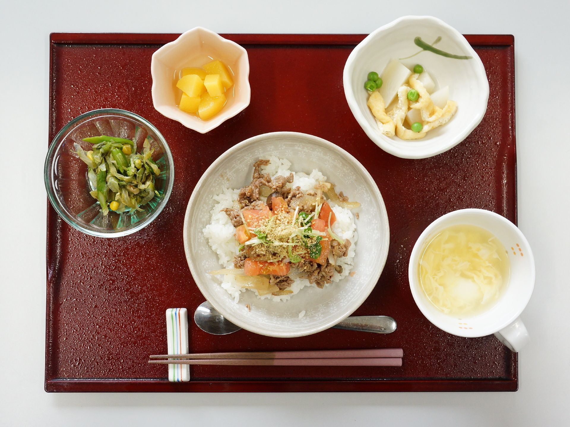 赤いトレーの上に食事メニューがセットされている。一番手前には箸置きに箸が置かれ、複数の食器が並べられている。