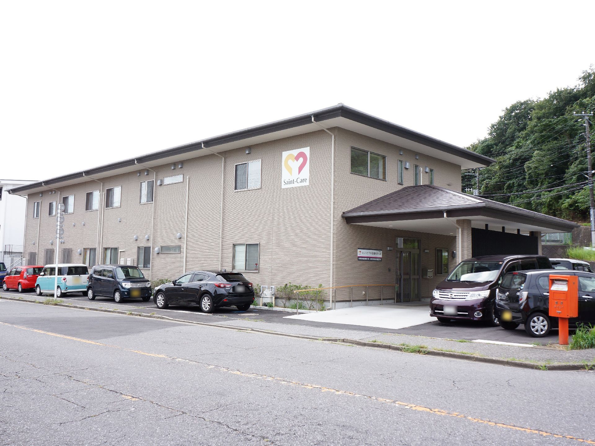 施設の建物は2階建てで、左側には大きな屋根がせり出している。壁はベージュ色で、2階部分に施設のロゴマークが付いている。