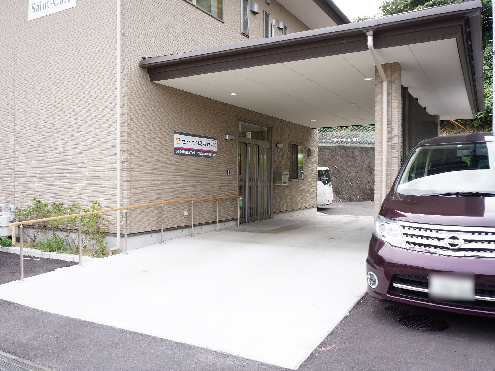 施設の入り口前には上部に大きな屋根が設置されている。右側には仕切り用の壁が設けられ、外側は駐車スペースになっている。