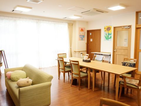 リビングの左側の壁には大きな窓があり、レースと厚地のカーテンが掛かっている。フロアにはテーブルセットが置かれている。