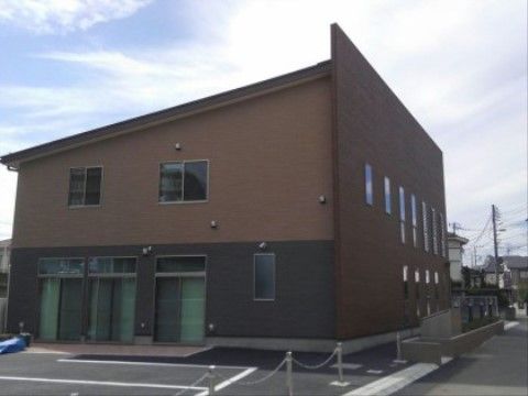 施設の建物は２階建てで、道路に面している。側壁の色は茶系とグレー系の配色で、建物の横には駐車場が設置されている。