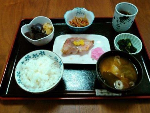 膳の上には、茶碗によそわれたご飯、焼き魚など副菜が２品、きんぴらごぼうの小鉢、漬け物、味噌汁、お茶、箸が置かれている。