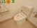 白色の壁に茶色のタイル調の床のトイレである。壁際には手すりが設置されている。便器の蓋や壁にはウサギやカエル、花のシールが貼られている。