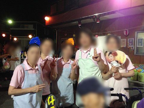 夜の野外イベントでピースをする、エプロン姿の5人の職員
