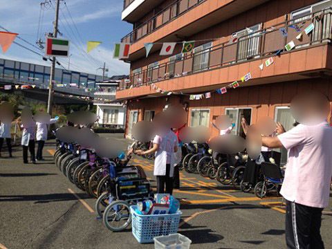 快晴の中屋外で手の体操をする車椅子の入居者とヘルパー