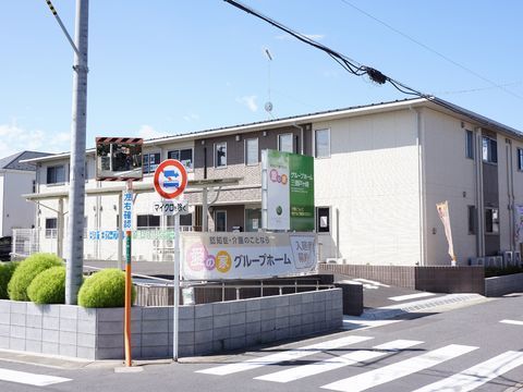 道路に面したベージュ色と焦げ茶色の外壁の2階建ての建物である。低いブロック塀が設けられ、看板が掲げられている。