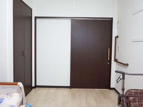 白色の壁と木目の床、焦げ茶色の引き戸の出入口の内装である。ドアの傍には茶色のエル型の手すりが設置してある。