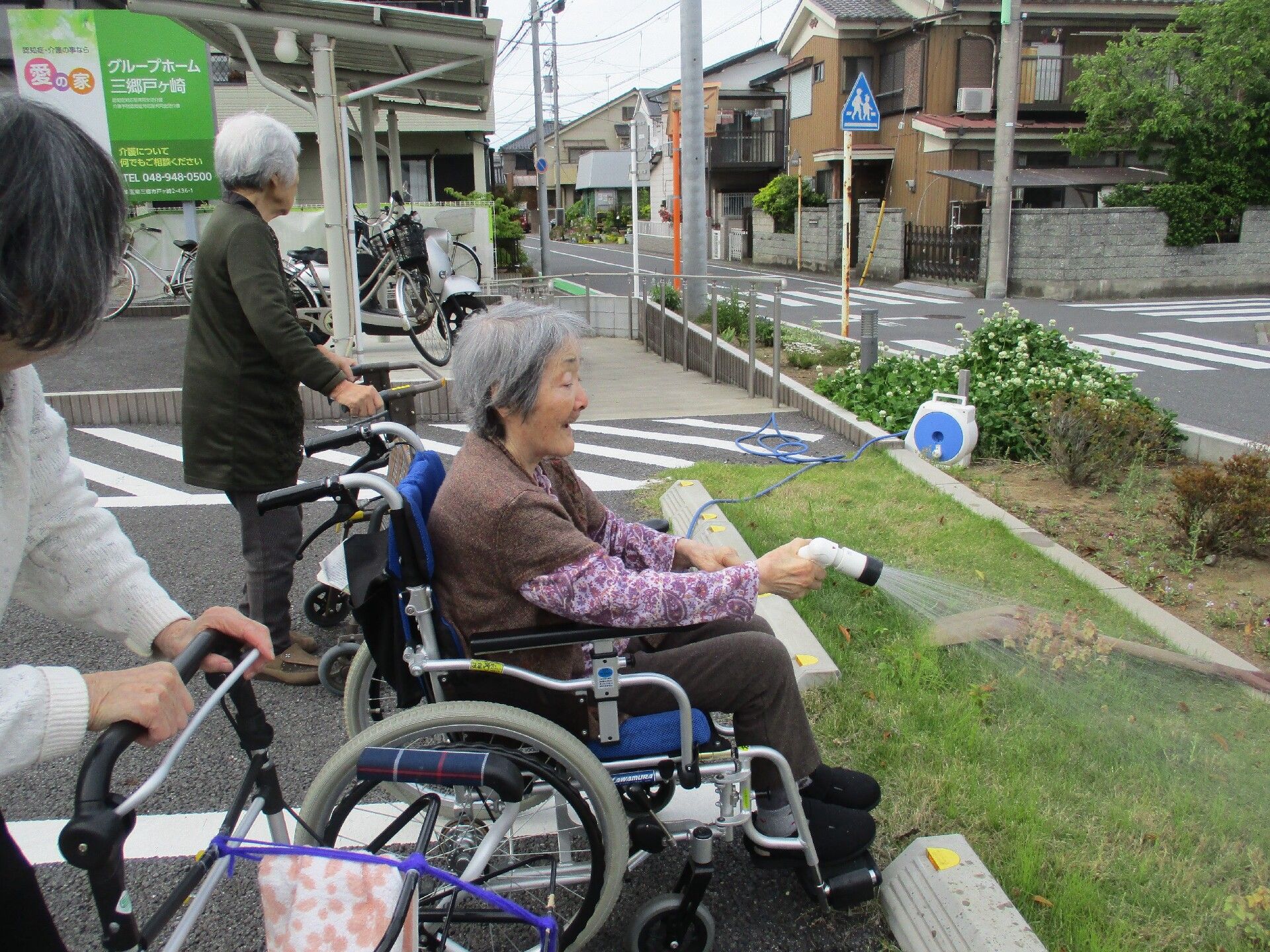 施設駐車場の芝生にホースでお水を撒く車椅子の入居者