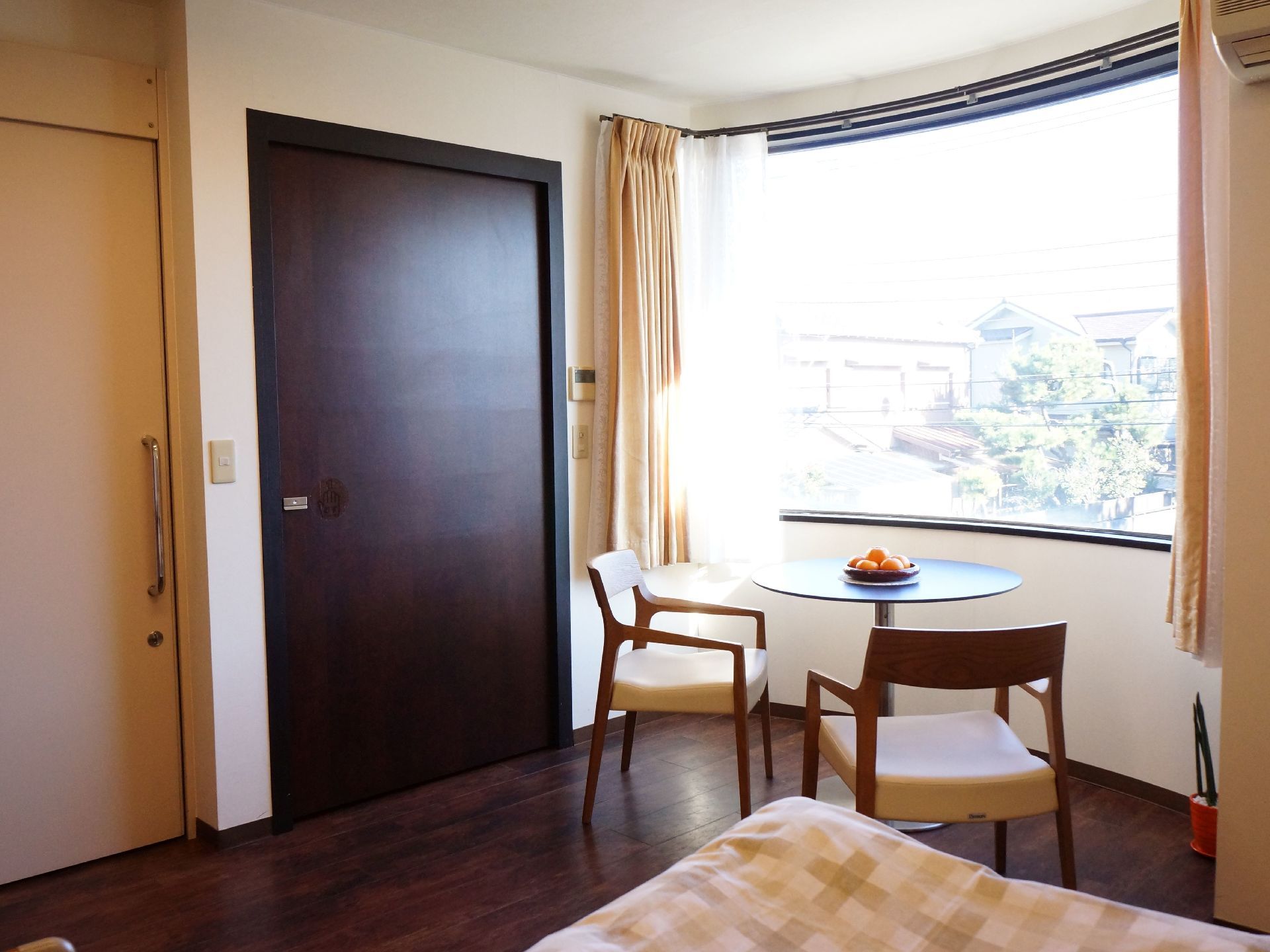 大きな円形の窓の前には丸いテーブルと椅子が２脚置かれている。部屋のドアは引戸タイプ。足元は木目調になっている。