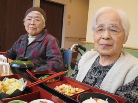 施設のお食事が並ぶテーブルの前でにっこり微笑む入居者