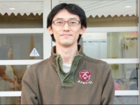 優しそうに微笑みながら施設の前に立っている男性ヘルパー