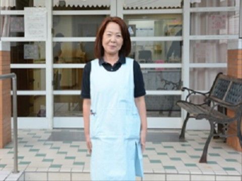 施設の玄関前でにっこりと微笑みながら立っている女性ヘルパー