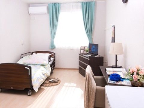 日当たりのよい環境に恵まれた居室である。ナースコールや介護用ベッド、エアコン、机、チェスト、テレビが完備されている。