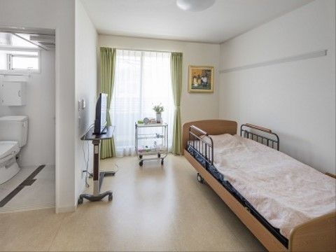 窓が大きく日当たりがよく、壁には絵が飾られている。移動式のキャスター付きの棚もあり、テレビも設置されている。