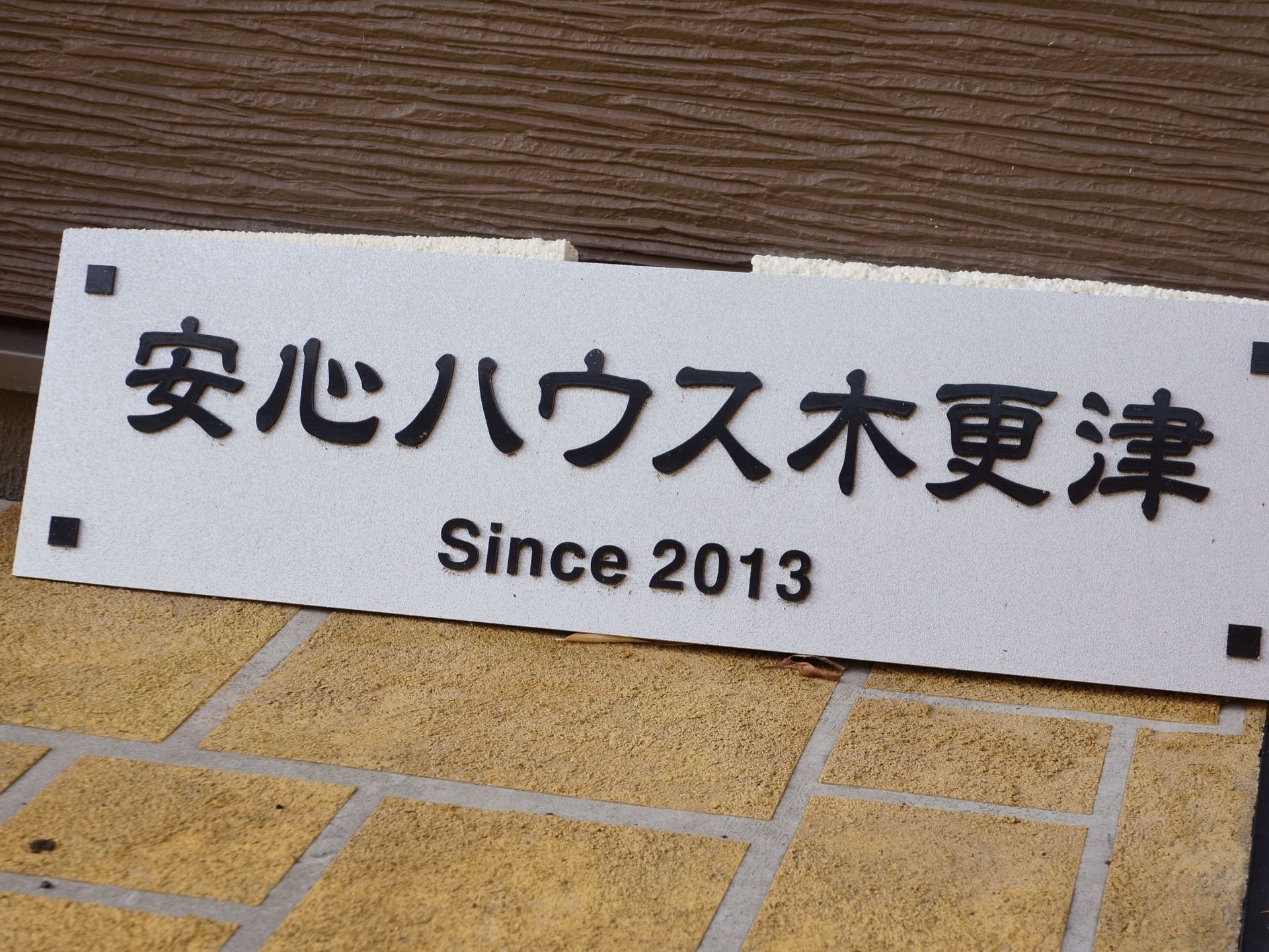 玄関の玄関の横にブロック調でできた施設看板を置いている。自然な形で設置しているが、目印になる看板になっている。