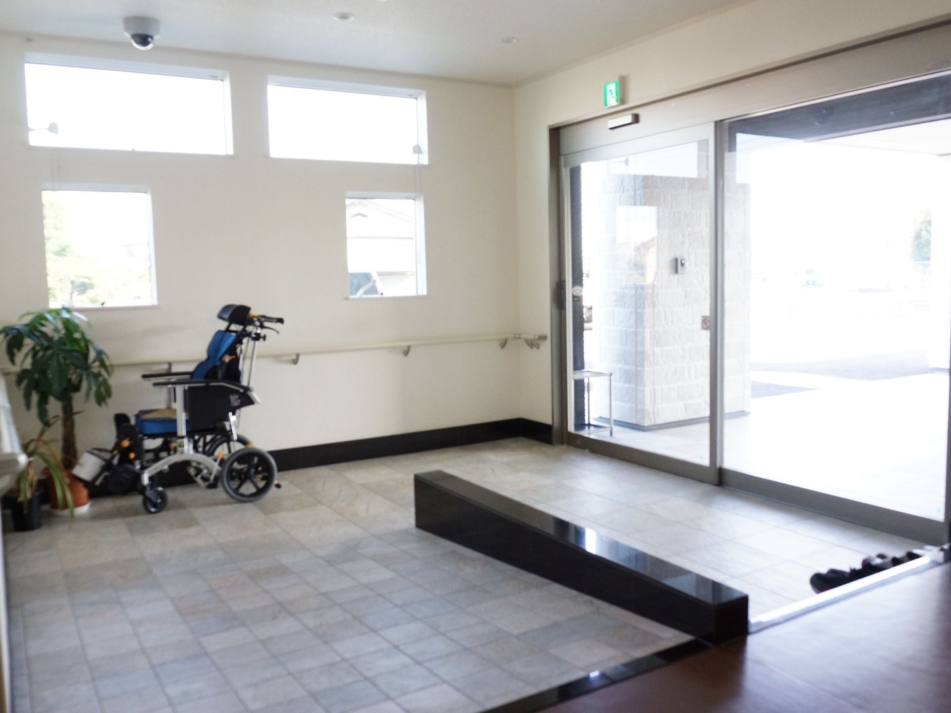 窓の多い明るい玄関には、車椅子でもストレスなく出入りできるように幅の広いスロープを設置している。壁には手すりが取り付けられている。
